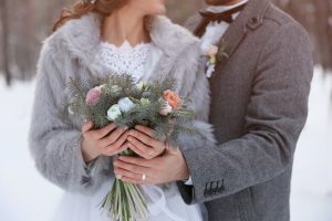 winter wedding shot of couple outside with their flowers and jackets