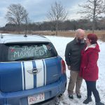 newlyweds smiling and looking at each other next to their car after drive-thru wedding