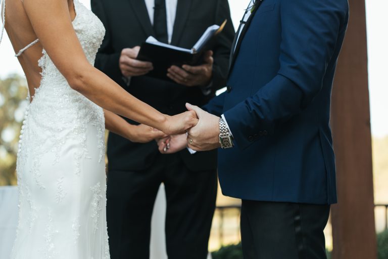 Bride and groom at ceremony outdoors, facing each other with a wedding officiant.
